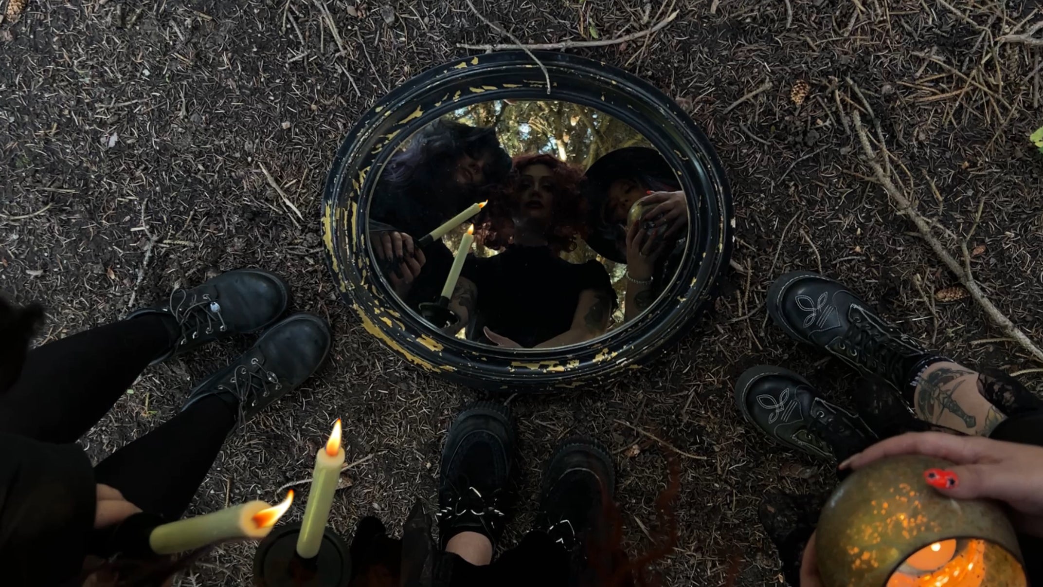 3 mystical witches scrying into a mirror on a forest floor